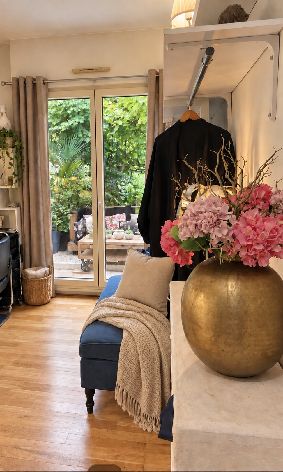 La banquette bleue du salon avec son coussin et son plaid beige, face au jardin